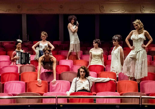 Promotional image : Deep red chairs of a theatre auditorium are filled with eight women; standing, leaning, sitting, balancing. Their eyes are fixed on us. Costumes span decades but all are feminine, sexy and ivory coloured. One woman has an accordion.