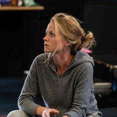 an image of Rachel looking off camera, in thought, mid rehearsal. Grey hoodie, messy hair.